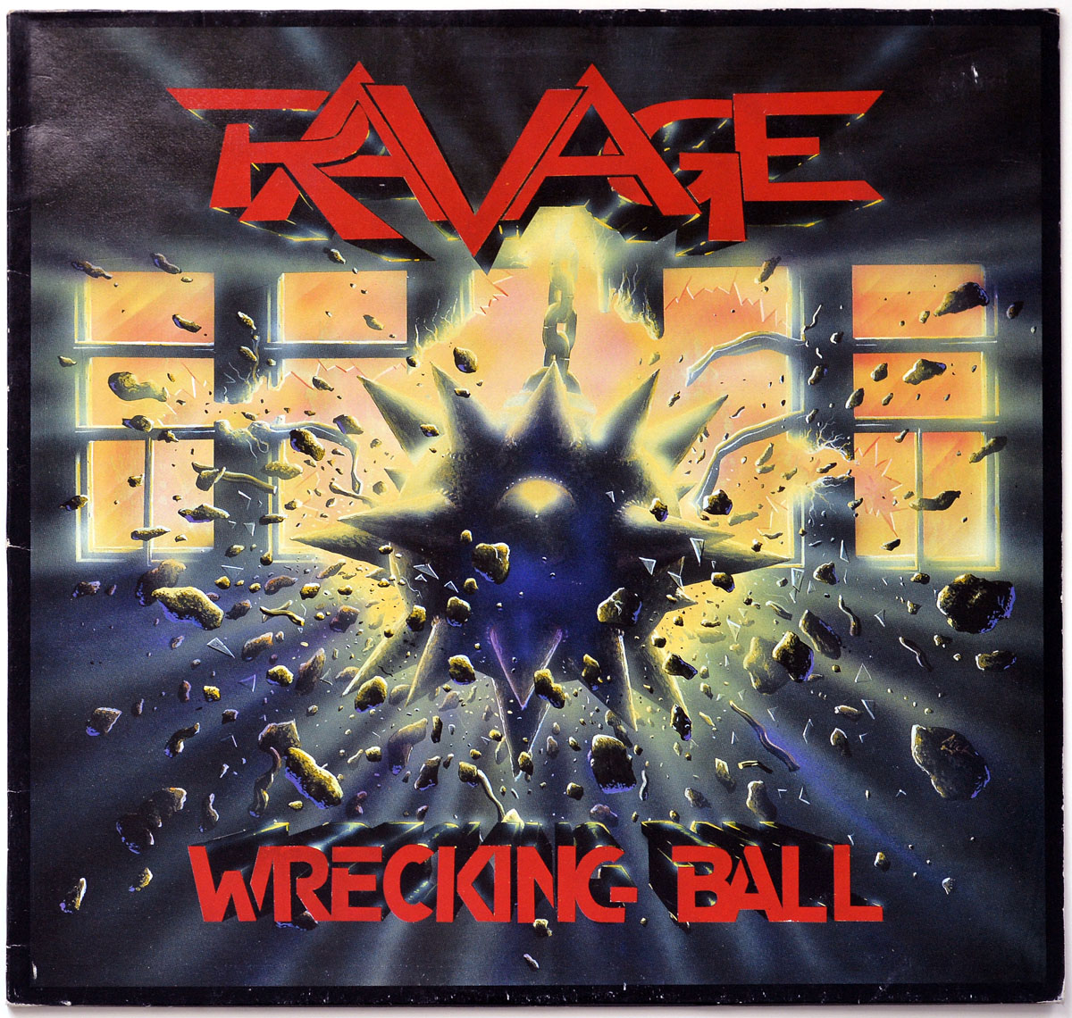 Front cover of RAVAGE - Wrecking Ball 1986 LP showing a spiked wrecking ball smashing through a brick wall, with bright yellow and purple explosive energy and debris flying in all directions